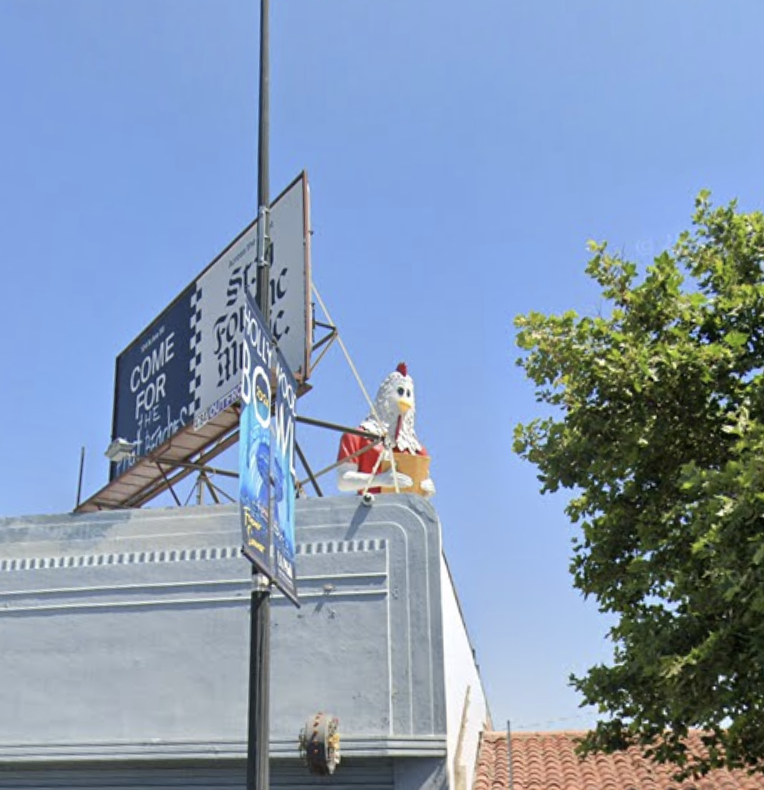 Chicken statue perched on a rooftop next to a billboard reading COME FOR THE.