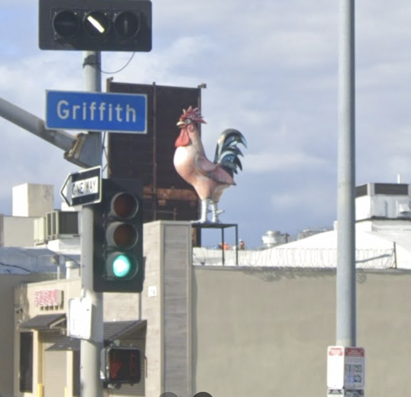 Rooster statue on a rooftop next to a Griffith street sign.
