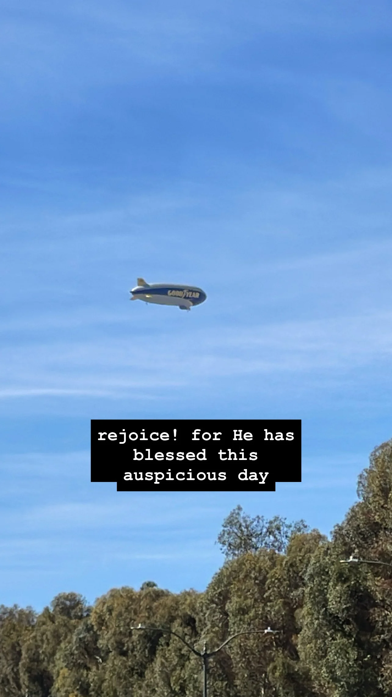 A plane or blimp flying across a clear blue sky. Caption: rejoice! He has blessed this auspicious day.