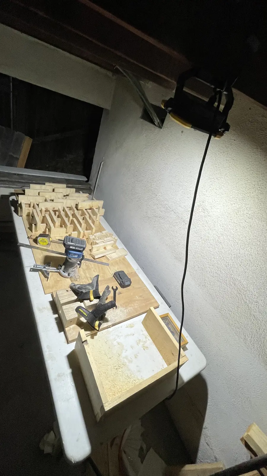 A construction work light clamped to a ceiling beam above a small workbench of wood offcuts and a router.