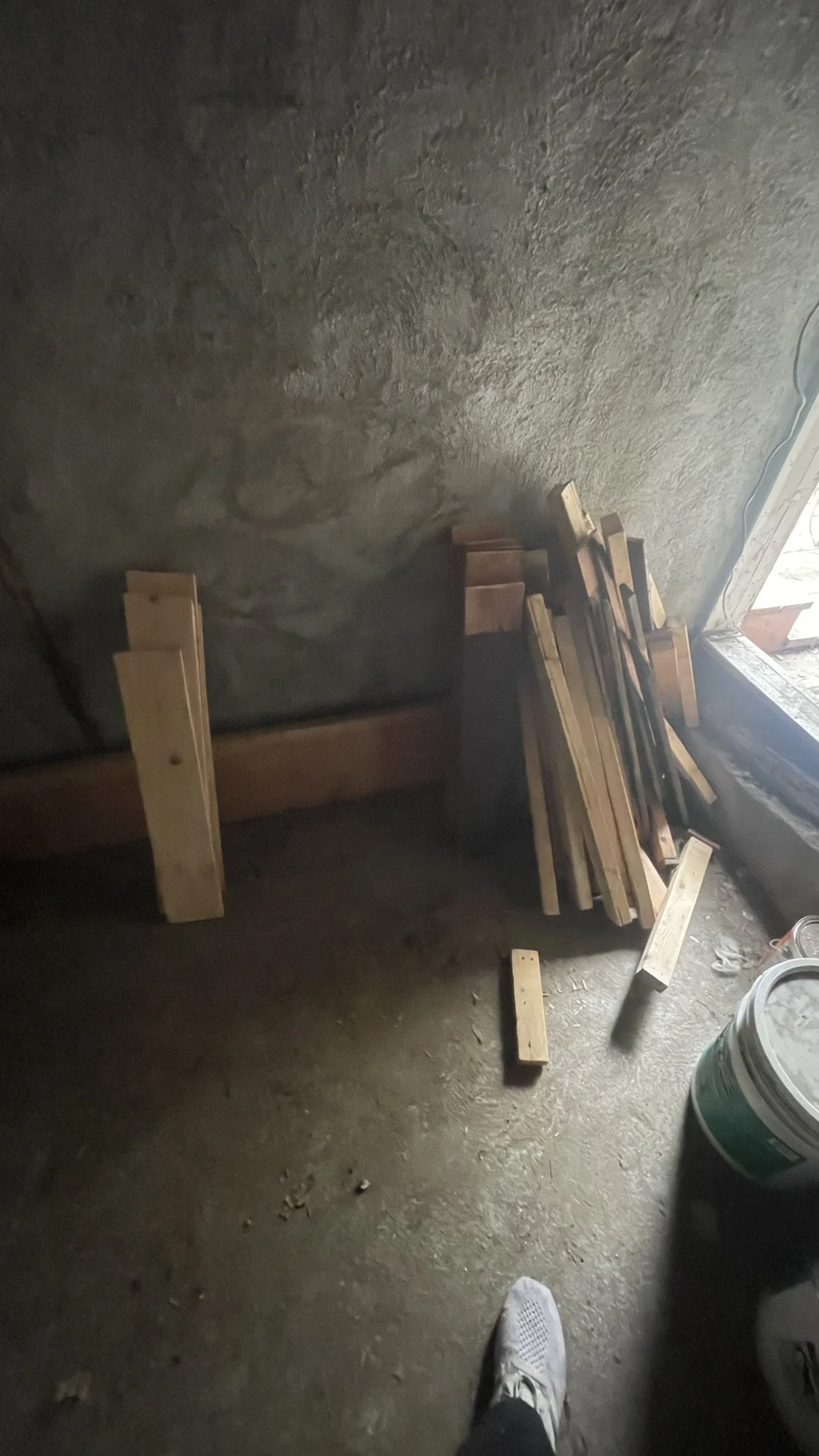 Wood planks leaning against a concrete wall inside the shed, lit by a work light.