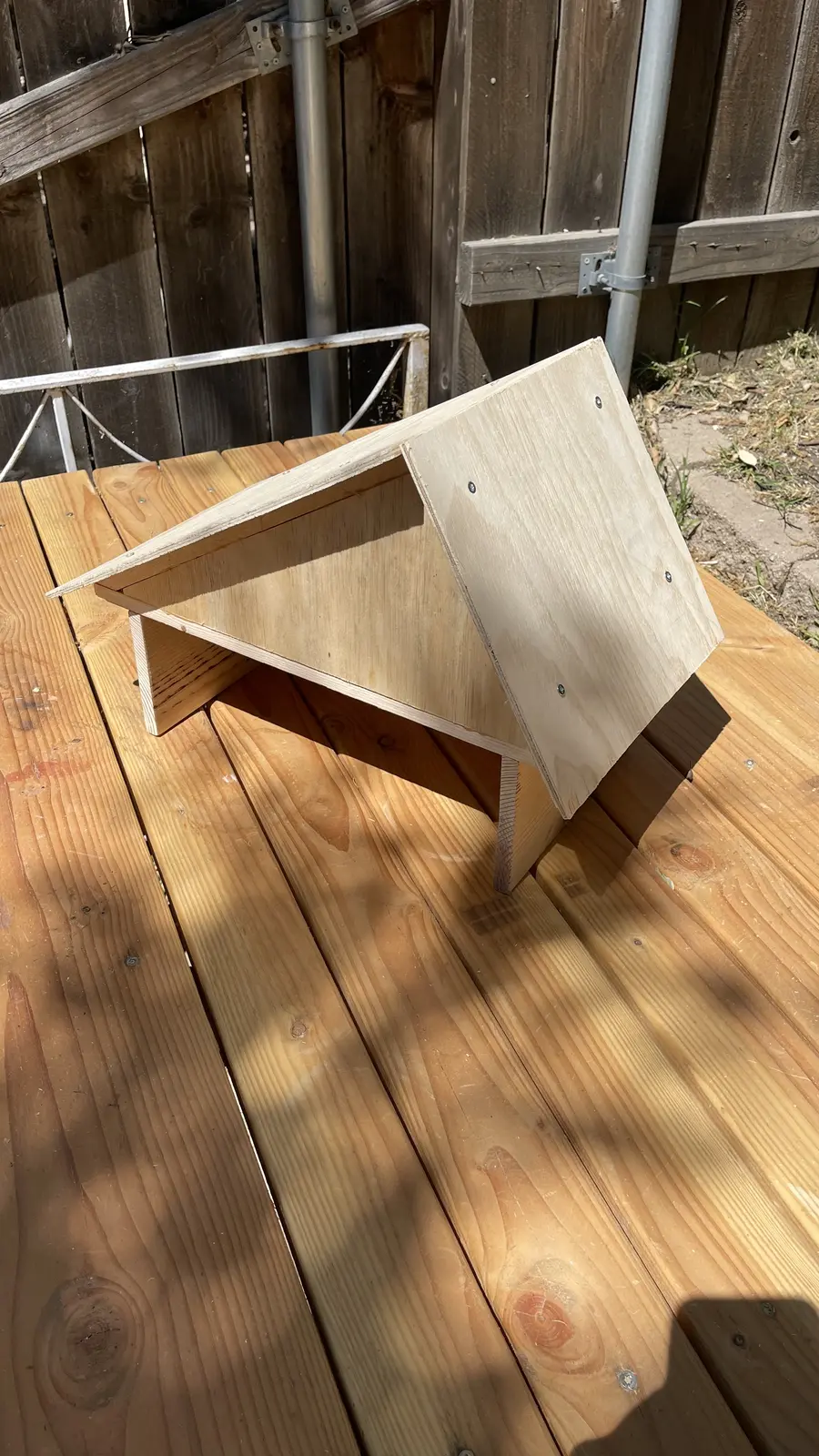 The finished small A-frame wood structure, doghouse-shaped, sitting on a wooden deck.
