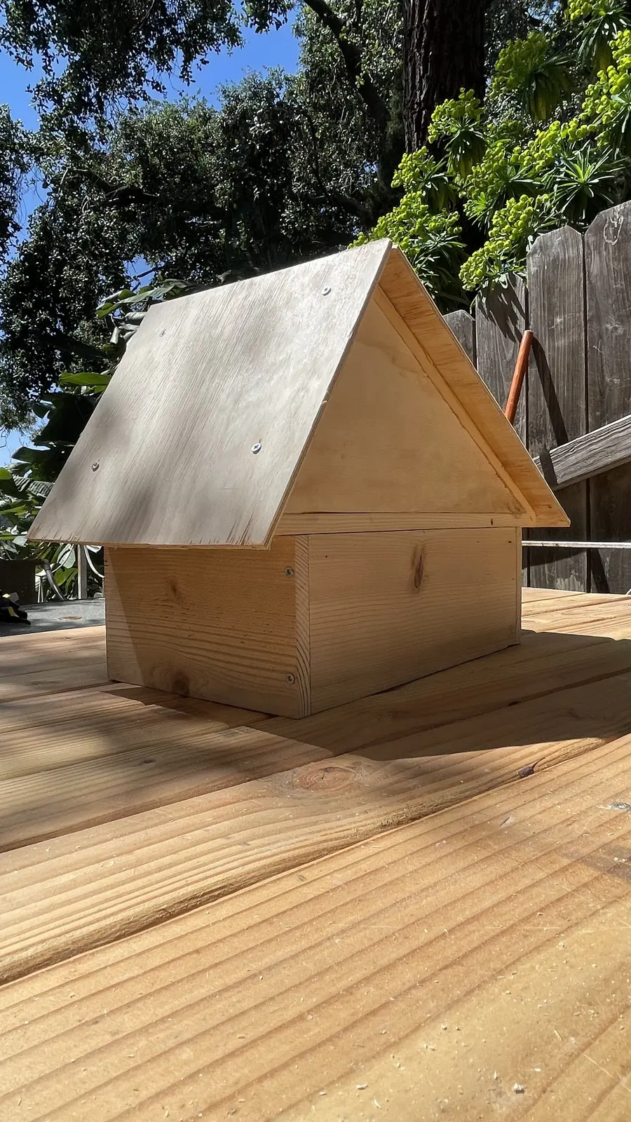 The finished A-frame wood structure from another angle, outdoors under trees.
